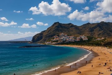 Spiaggia di Tenerife con sabbia dorata e mare turchese, circondata da montagne e villaggi costieri, fotografata in alta definizione al tramonto.