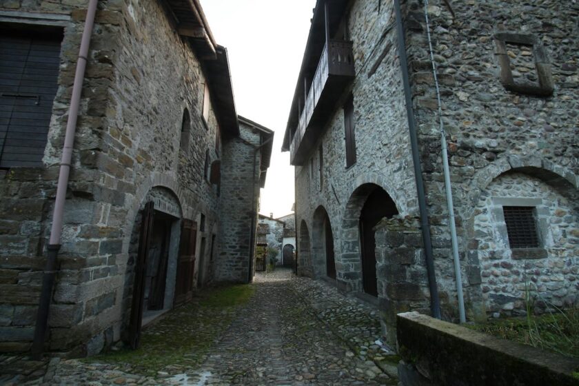 Borgo medievale lombardo con case in pietra e campanile immerso tra colline verdi